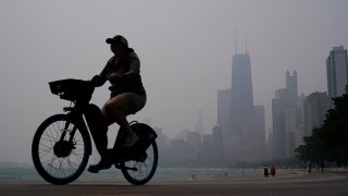 A person rides a bicycle along the shore of Lake Michigan as the downtown skyline is blanketed in haze from Canadian wildfires, June 27, 2023, in Chicago.