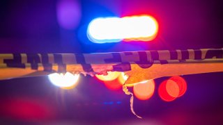 A defocused police car sits behind crime scene tape with flashing lights at night.