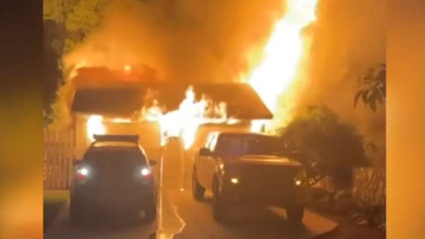 Fire engulfs a home as two cars park on the driveway.