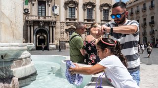 A little girl wets her hat because it is too hot in the Elephant Fountain in Piazza Duomo while her father wets his head on July 15, 2023 in Catania, Italy.