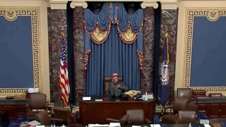 This image from U.S. Senate video, introduced at the trial of Bruno Joseph Cua, shows Cua sitting with his feet up in the Senate chamber on Jan. 6, 2021, during the riot at the U.S. Capitol.