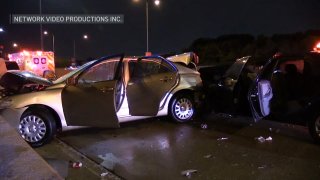 A silver sedan with a badly-damaged hood and rear left panel is seen resting against a concrete retaining wall, with a Chicago fire ambulance in the background.