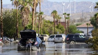 Dorian Padilla sits in his car as he waits for a tow after it got stuck in the mud on a street Monday, Aug. 21, 2023, in Cathedral City, Calif.