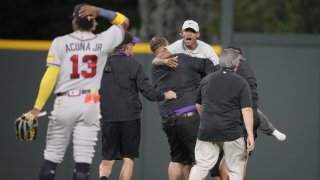 Atlanta Braves right fielder Ronald Acuna Jr., bottom center, ends up on the turf as guards wrestle down two fans who approached him as he took his spot in the field for the bottom of the seventh inning of a baseball game against the Colorado Rockies.