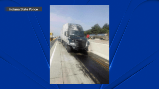 A silver semi truck, carrying a white trailer, is seen splattered with tar after a significant crash on the Indiana Toll Road Aug. 22, 2023. Tar is also seen all over the pavement in front of the truck.