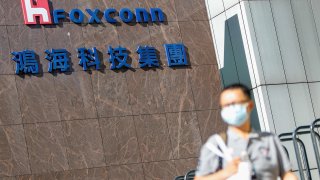 A man with a face mask walks past the logo of Foxconn, or Hon Hai Group , which is Taiwans technology giant and the worlds leading producer of semiconductors or chips particularly for Apples devices, amid COVID-19 outbreak , in Taipei, Taiwan, 15 July 2021.