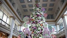 A towering Christmas tree, loaded for bear with white snowflakes and purple and green ornaments, and fronted by two purple and green Nutcracker figures, stands in the Macy's Walnut Room in Chicago. The room features vaulted ceilings with blue tiles and white framing, and the whole room is surrounded by large windows.
