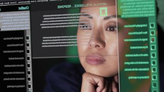 Stock image showing an Asian woman studying a see through screen which is producing lines of AI generated text. A ChatBot similar to A.I. is being read attentively by this woman.