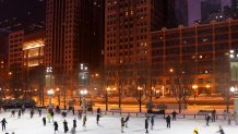 Snowing winter night in the center of Chicago. Twilight street view with ice rink on a foreground, trees decorated by glowing holiday garlands and skyscrapers on a background. Urban architecture.