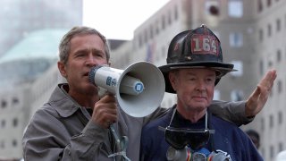 US President George W. Bush (L), standing next to retired firefighter Bob Beckwith, 69, speaks to volunteers and firemen as he surveys the damage at the site of the World Trade Center 14 September 2001 in New York. AFP PHOTO/Paul RICHARDS (Photo by Paul J. RICHARDS / AFP) (Photo by PAUL J. RICHARDS/AFP via Getty Images)