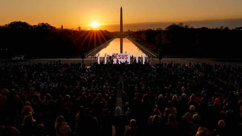 The word "Jesus" is displayed on a large monitor and worship songs are played on stage as people gather for the "Easter Sunrise Service" at the Lincoln Memorial