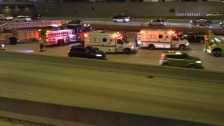 Multiple white Chicago Fire Department Ambulances and multiple red Chicago fire trucks surround a collision site on the Dan Ryan Expressway, with vehicles passing in the foreground behind a cement wall.
