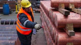 An employee scans barcodes on copper rods as they sit stacked outside at the Aurubis AG headquarters in Hamburg, Germany.