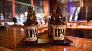 Four bottles of Lagunitas IPA, with white labels and black font, are shown on a platter, resting on top of a brown-wooden bar.