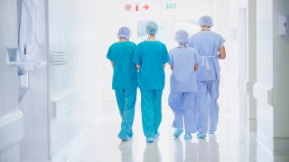 Rear view of four medical staff wearing scrubs walking in hospital corridor