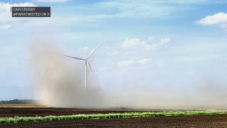A dust storm blows across a farm field in central Illinois, partially obscuring a wind mill.