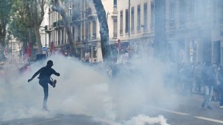 A demonstrator dressed all in black kicks back with his foot a puck of tear gas fired by police in their direction, during a demonstration against fascism and the National Rally party, in Lyon, France, June 16, 2024. 