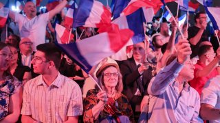 Supporters fly french flags as former president of the French far-right Rassemblement National (RN) parliamentary group Marine Le Pen gives a speech during the results evening of the first round of the parliamentary elections in Henin-Beaumont, northern France, on June 30, 2024. 