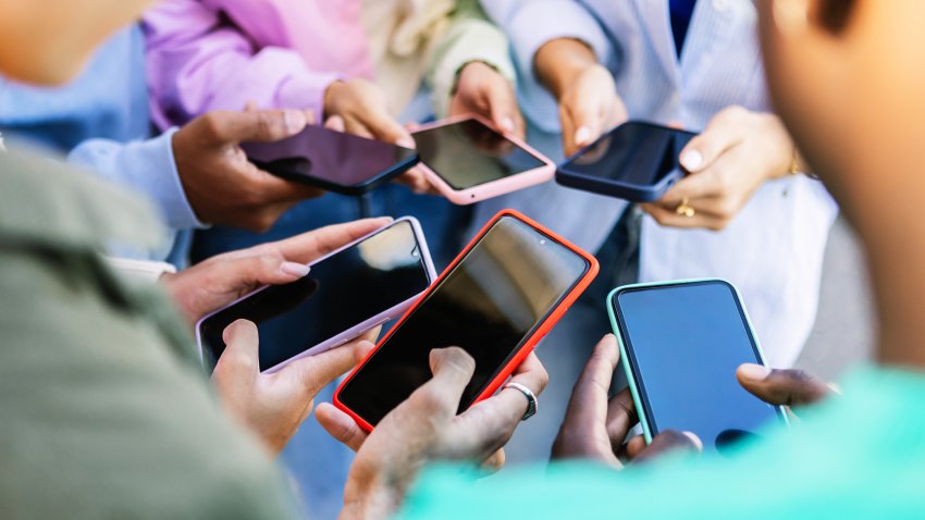 Young group of people standing in circle using mobile phones outside. Unrecognizable teen friends watching social media content on smartphone app. Technology lifestyle concept.