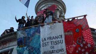 Participants gesture as they stand with a giant banner which reads as “France is the fabric of migration” during an election night rally following the first results of the second round of France’s legislative election, at Place de la Republique in Paris on July 7, 2024.