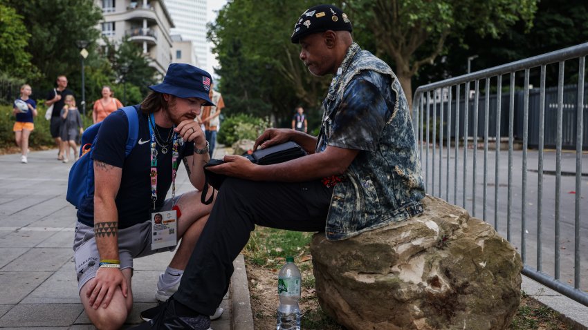 An accredited personnel browses through a collection of the pin trader outside the athletes’ village in Saint-Denis, ahead of the Paris 2024 Olympic Games on July 21, 2024.