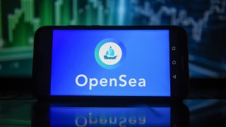 In this photo illustration an OpenSea logo is displayed on a smartphone with stock market percentages in the background.