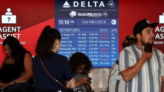 Travelers wait in line, as a flight board shows delays, on the check-in floor of the Delta Air Lines terminal at Los Angeles International Airport (LAX) on July 23, 2024 in Los Angeles, California. 