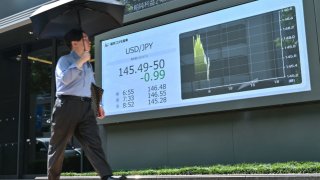 A pedestrian walks past a display board showing the currency exchange rate between the US dollar and the Japanese yen, along a street in Tokyo on August 5, 2024.