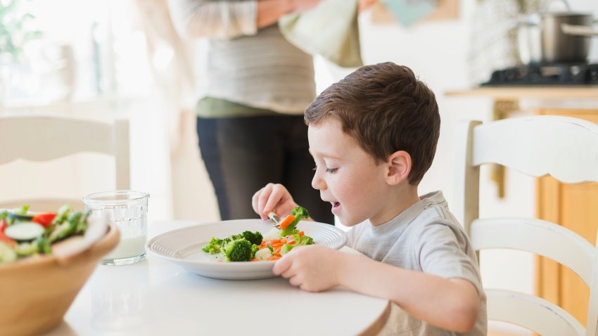 A boy eating vegetables at the dinner table.