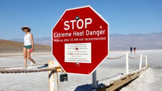 Visitors walk near a ‘Stop Extreme Heat Danger’ sign in Badwater Basin salt flats in the morning, when temperatures are less hot, during a long-duration heat wave which is impacting much of California on July 9, 2024 in Death Valley National Park, California.