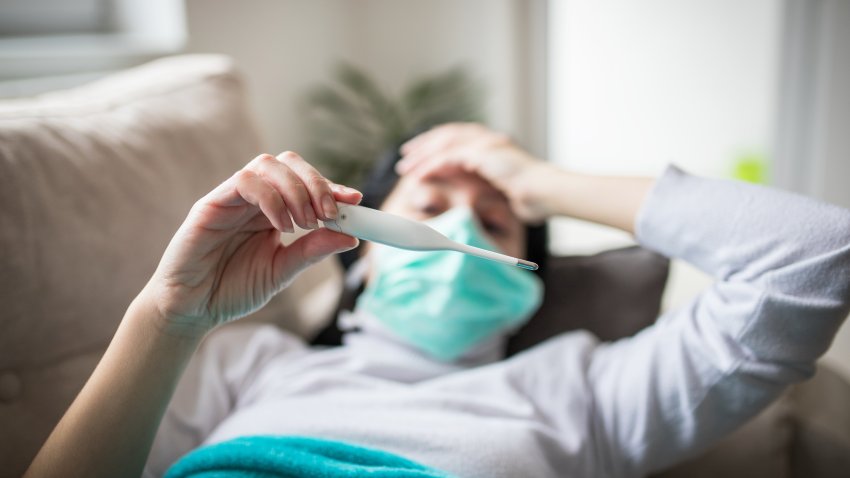 Ill infected woman checking thermometer having fever. Girl wearing protective mask while having cold.