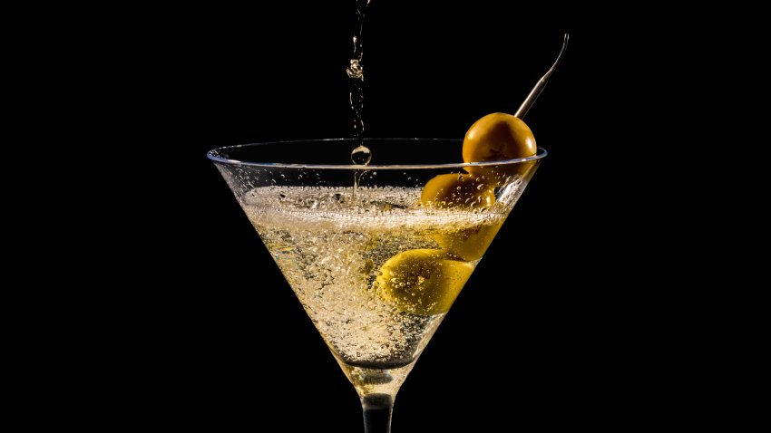 Pouring and splashing martini glass with green olives on a dark background. Selective focus and close up. Alcohol and artistic concept.