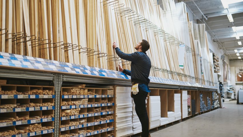 Young handyman selecting a length of cut timber from a rack in a hardware supply warehouse standing reaching up for his selection