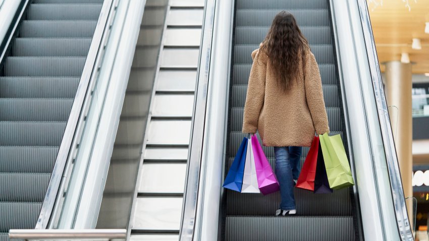 Back view of a woman holding shopping bags while standing on a escalator at mall center. Shop concept.