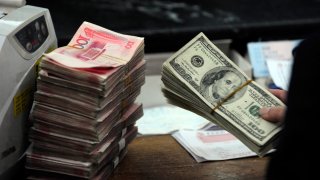 A Chinese bank worker prepares to count a stack of US dollars together with stacks of 100 Chinese yuan notes at a bank in Hefei, east China’s Anhui province on March 9, 2010.  