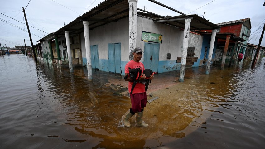 A man carries a dog as he wades through a flooded street after the passage of Hurricane Rafel in Batabano, Mayabeque province, Cuba, on November 7, 2024.