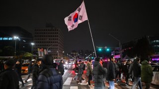 A man holds the South Korea flag outside the National Assembly in Seoul on December 4, 2024, after President Yoon Suk Yeol declared emergency martial law. South Korea’s President Yoon Suk Yeol on December 3 declared emergency martial law, saying the step was necessary to protect the country from “communist forces” amid parliamentary wrangling over a budget bill. 