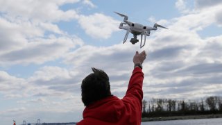 FILE – In this April 29, 2018, file photo, a drone operator helps to retrieve a drone after photographing over Hart Island in New York.