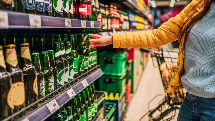 Woman customer in alcohol section in supermarket or liquor store holding a bottle from the shelf