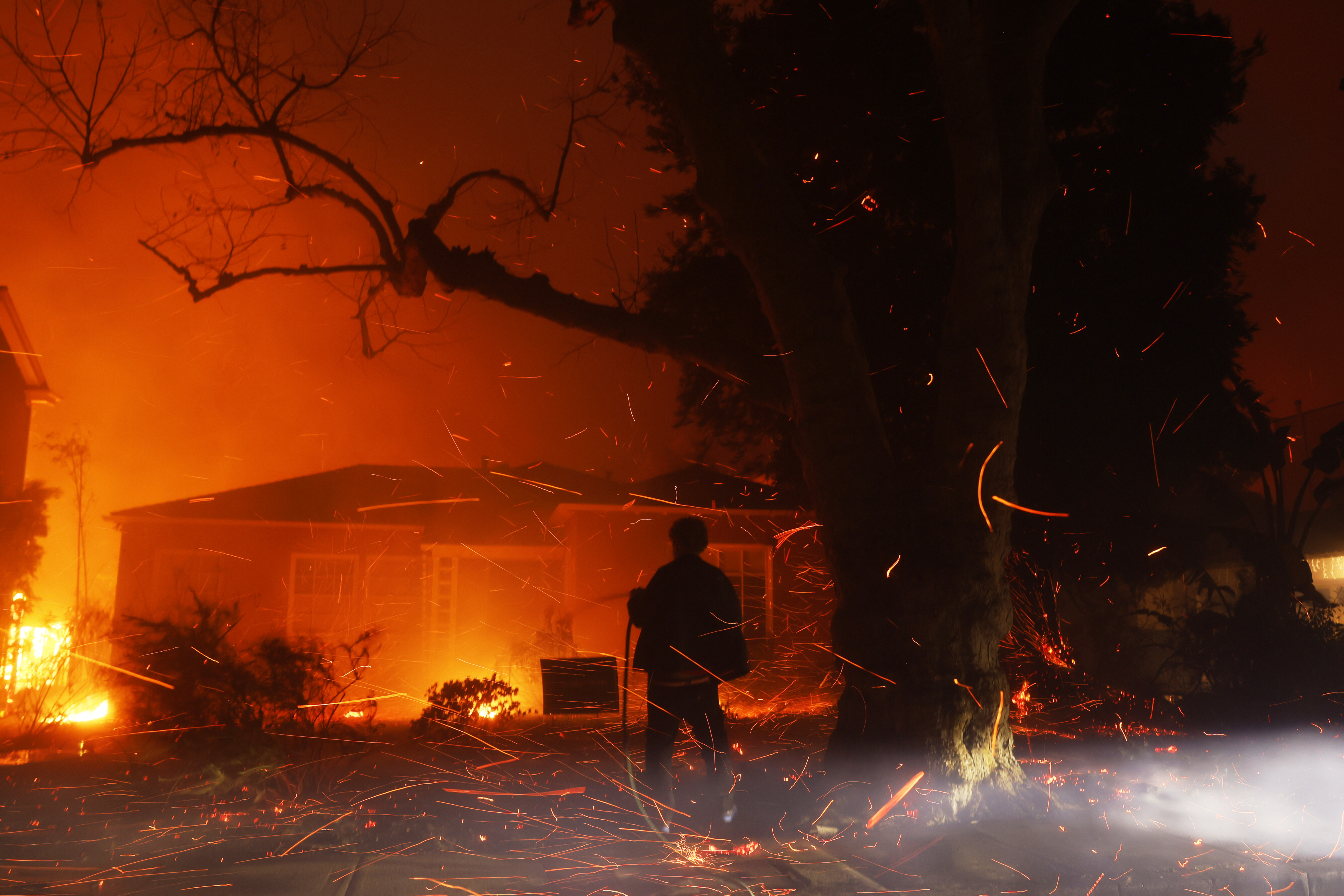 A person tries to hose down embers from the Palisades Fire in the Pacific Palisades neighborhood of Los Angeles, Tuesday, Jan. 7, 2025.