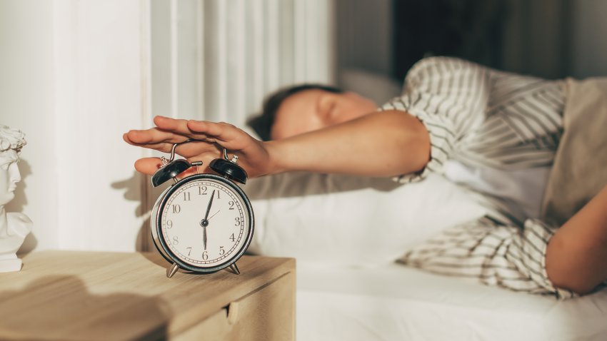 Young sleeping woman and alarm clock in bedroom at home