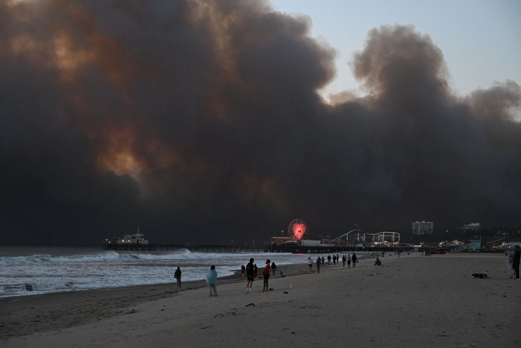 Smoke from the Palisades Fire fills the sky as seen from Santa Monica Beach, with the Santa Monica Pier and Ferris Wheel in the foreground on January 07, 2025 in Los Angeles, California.