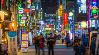 People walking through the neon lit night streets of Sinchon in the heart of Seoul, South Korea’s vibrant capital city.