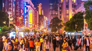 Crowds walk below neon signs on Nanjing Road. The street is the main shopping district of the city and one of the world’s busiest shopping districts.
