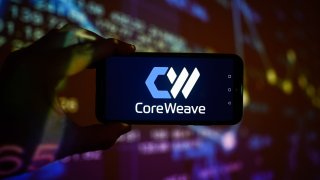 A CoreWeave logo is displayed on a smartphone with stock market percentages in the background.