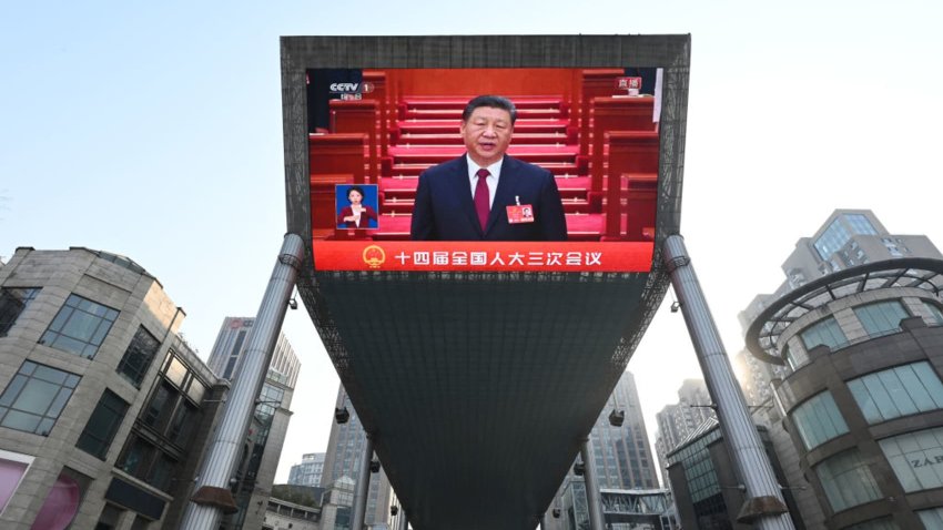 This photo shows a general view of a screen broadcasting live footage of China’s President Xi Jinping attending the opening session of the National People’s Congress (NPC) as seen outside a shopping mall in Beijing on March 5, 2025. 