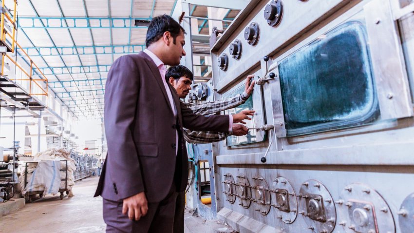 Business, India, Factory – Young Businessman with his factory floor supervisor inspecting the newly installed heavy machinery at a textile factory.