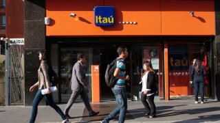 Pedestrians walk past an Itau Unibanco Holding SA bank branch in Sao Paulo, Brazil.