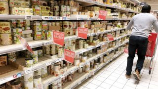 A man pushes his shopping cart filled with food shopping and walks in front of an aisle of canned vegetables with “Down price” labels in an Auchan supermarket in Guilherand Granges, France, March 8, 2025.