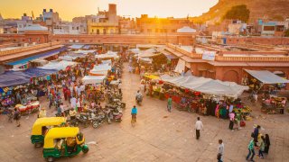 The beautiful market in Jodhpur’s Old City. People are visible in the image, walking standing or sitting in their rickshaws as it is the case in the foreground.